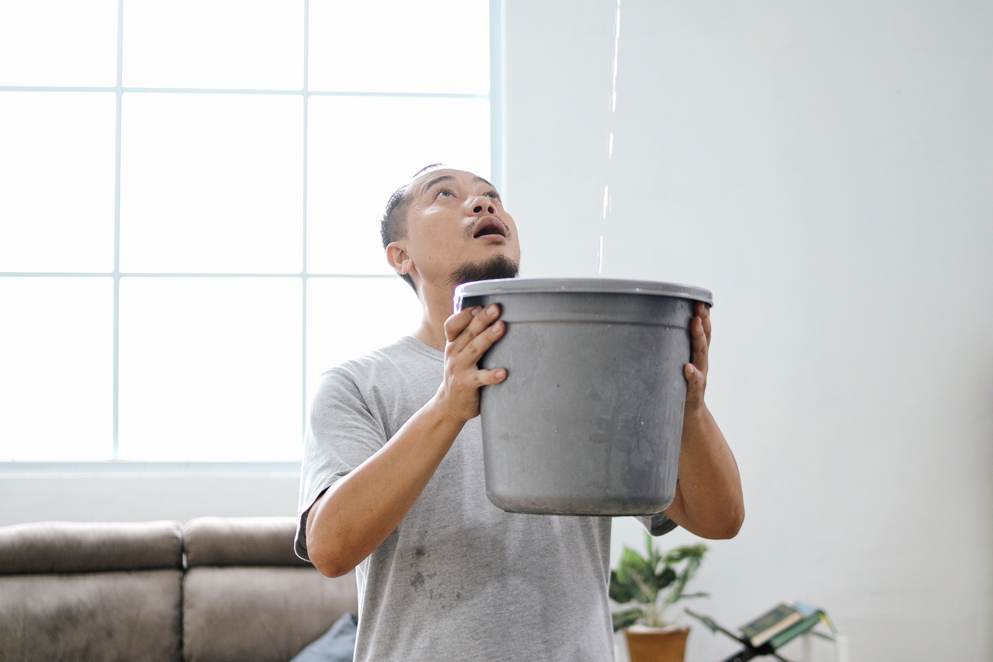Man Collecting Water From Damaged Roof