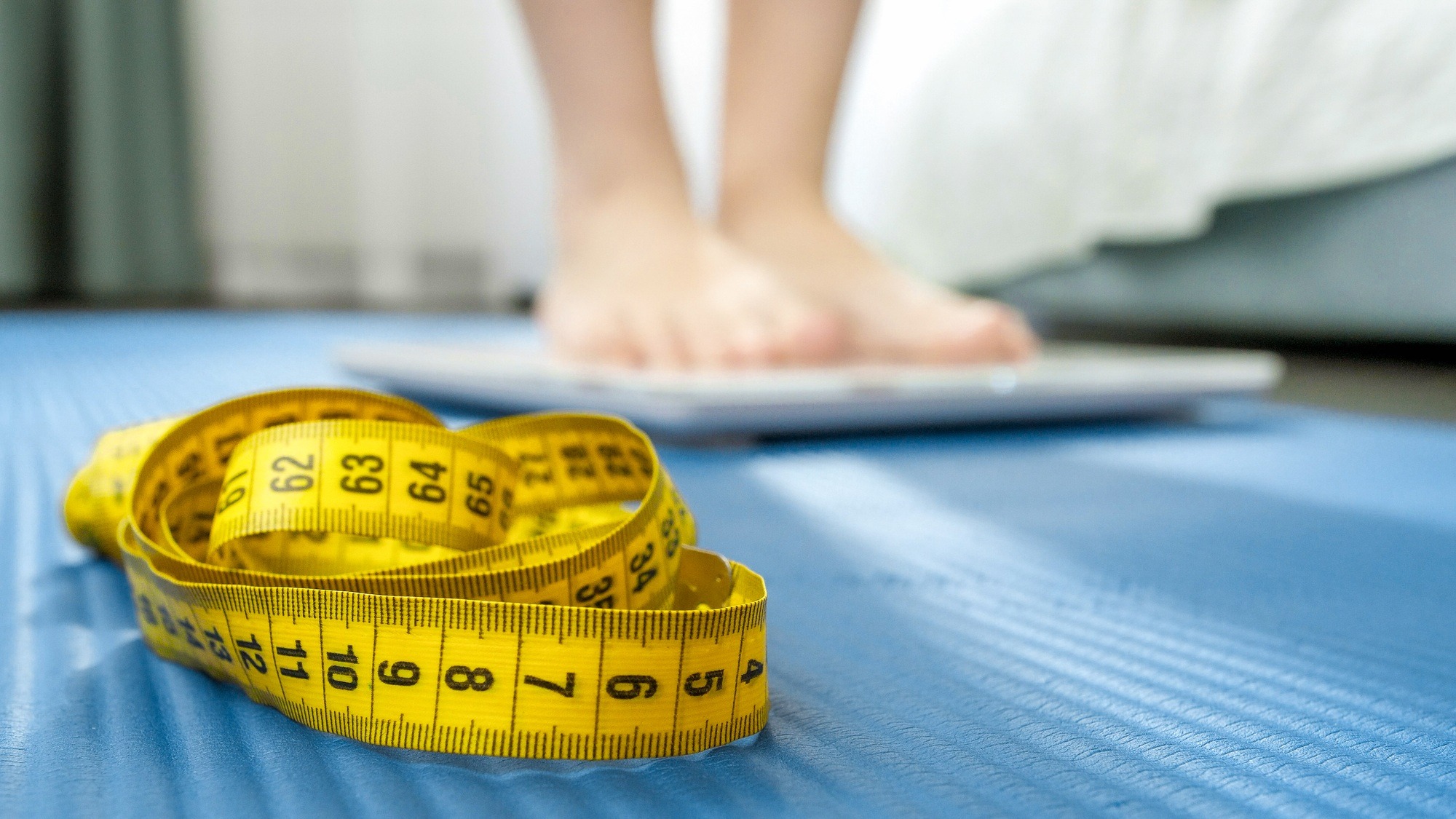 Measuring tape, fitness mat and young woman weighting on scales. Concept of dieting, sports, loosing