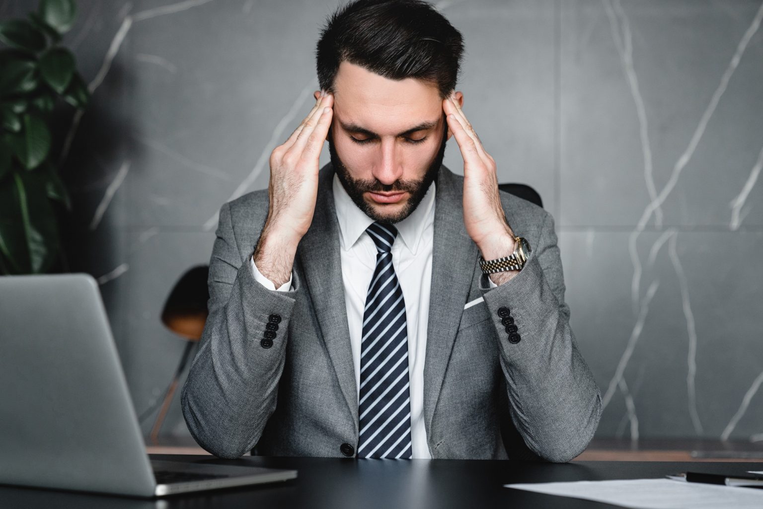 Stressed young businessman rubbing temples because of fatigue at workplace.