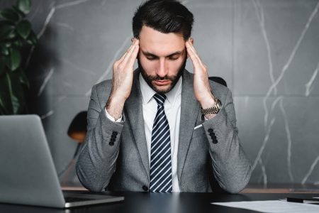 Stressed young businessman rubbing temples because of fatigue at workplace.