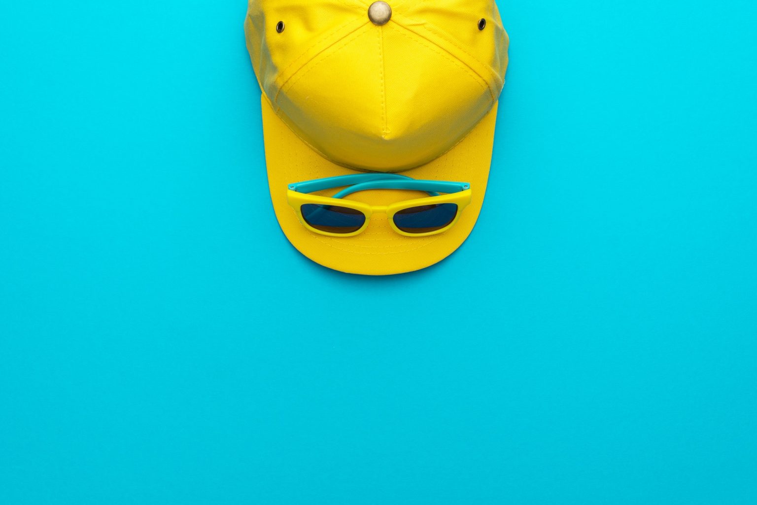 Yellow Baseball Cap And Sunglasses On Blue Background With Copy Space