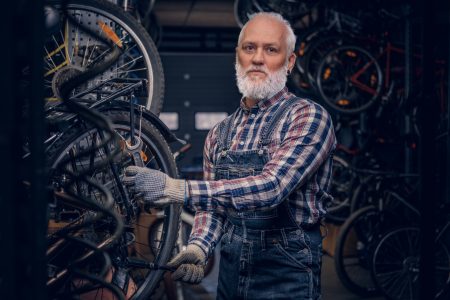 Elderly handyman dressed in plaid shirt and overalls around bikes