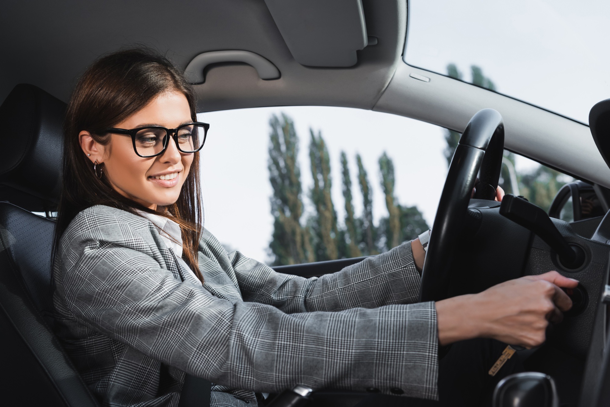 happy businesswoman in eyeglasses smiling while starting car