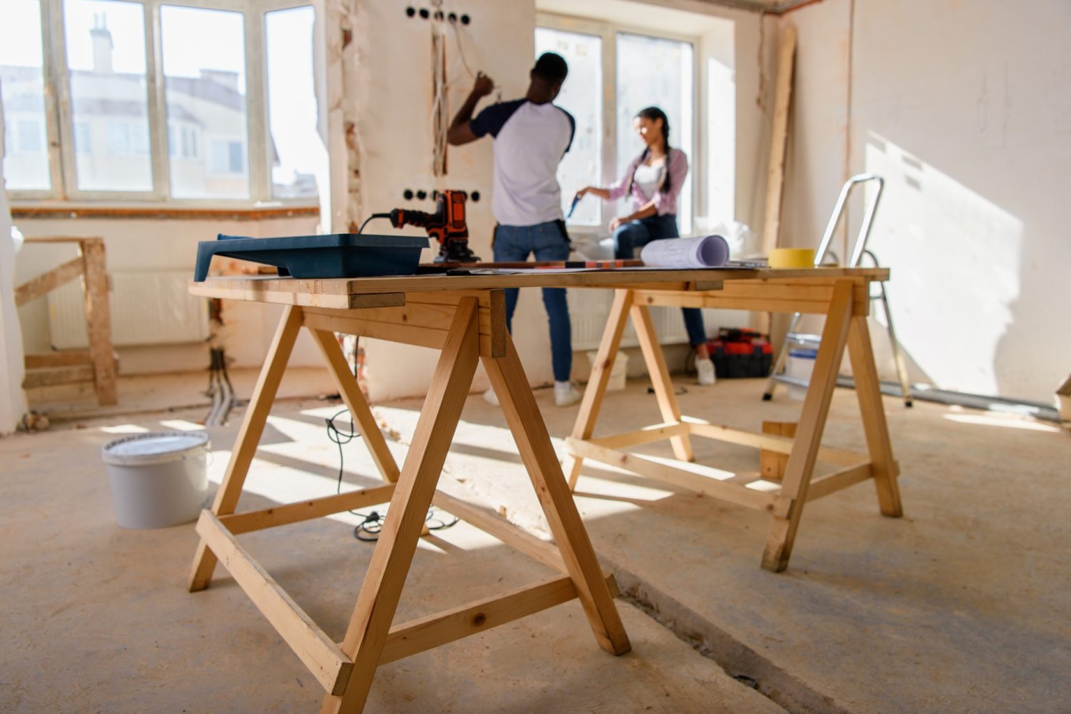 selective focus of wooden table with instruments and couple making renovation behind at home