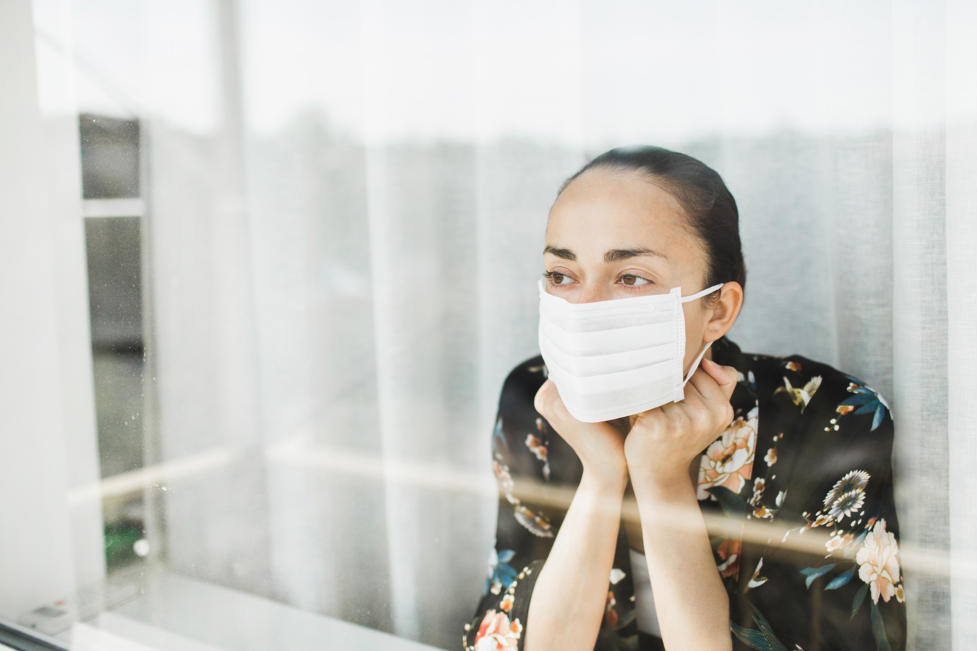 Self isolation in coronavirus quarantine. Woman in medical mask looking through window