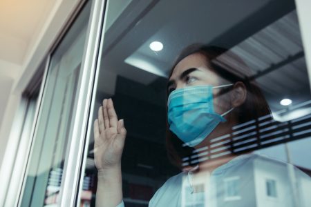woman looking through the window and wearing medical mask protection