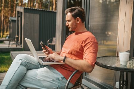 A young man with a laptop sitting outside and working online