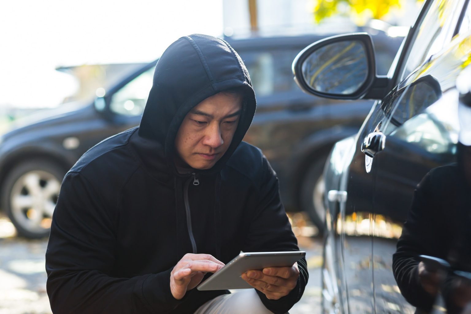male bandit thief car thief asian uses a tablet to turn off the car alarm