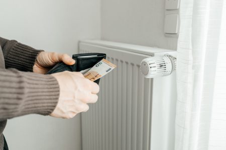 The man's hands hold a wallet with money next to the radiators.