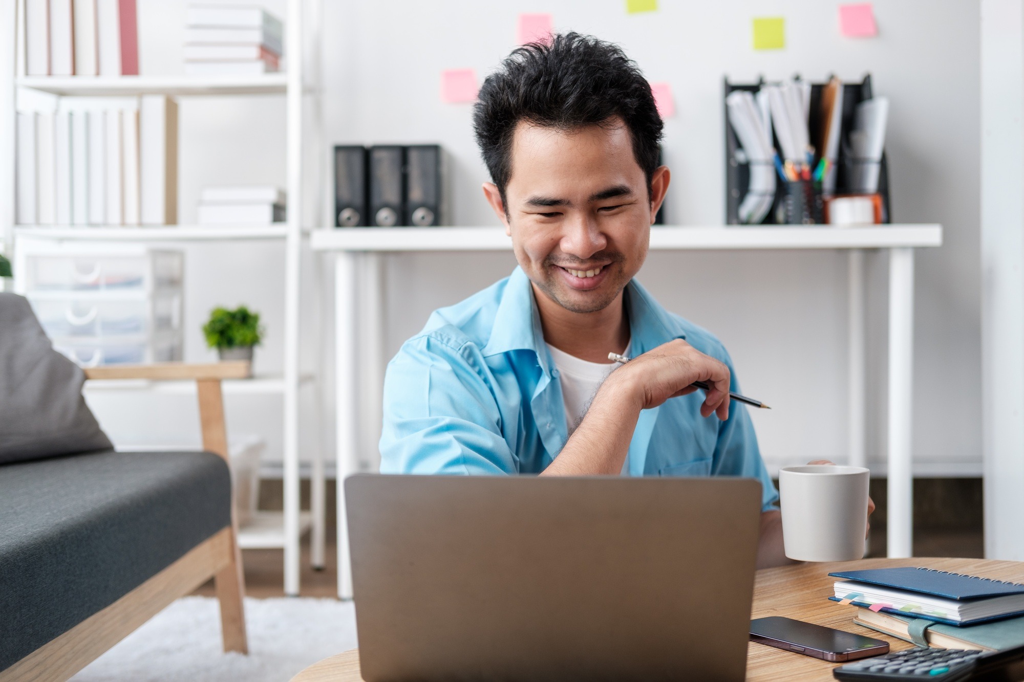 Young attractive man sitting on sofa at home working on laptop online, using internet, smiling,