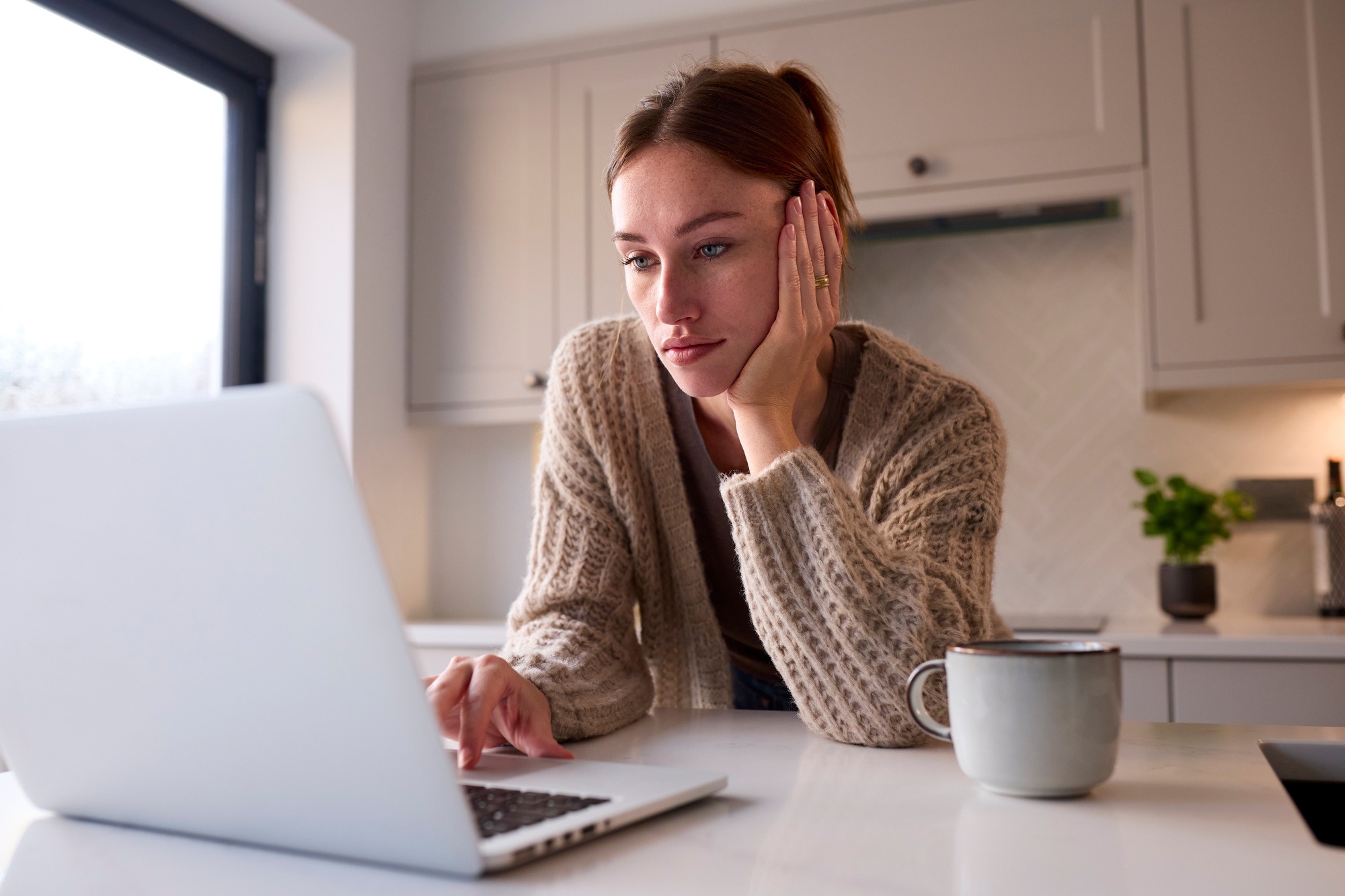 Young Woman At Home Working On Laptop On Counter In Kitchen