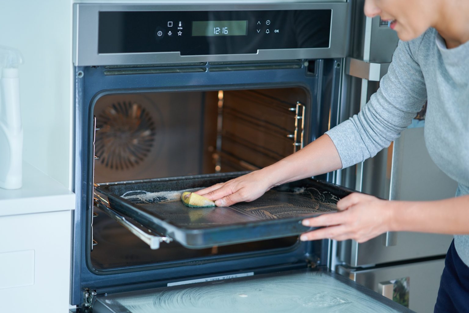 Young woman cleaning oven in the kitchen
