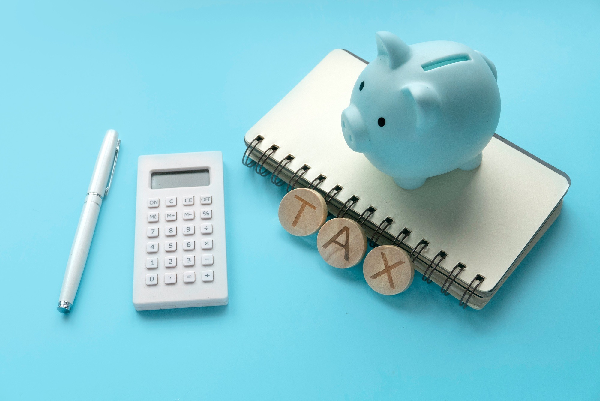 Tax concept. Pen, calculator, piggybank and notebook on blue background.