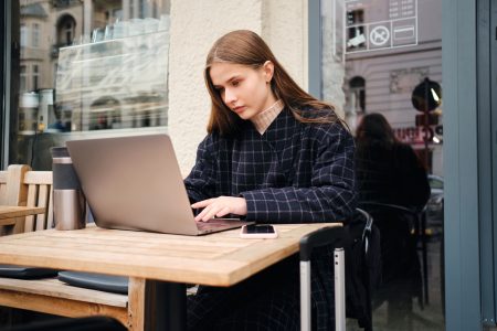 Beautiful girl searching place to stay on laptop in street cafe