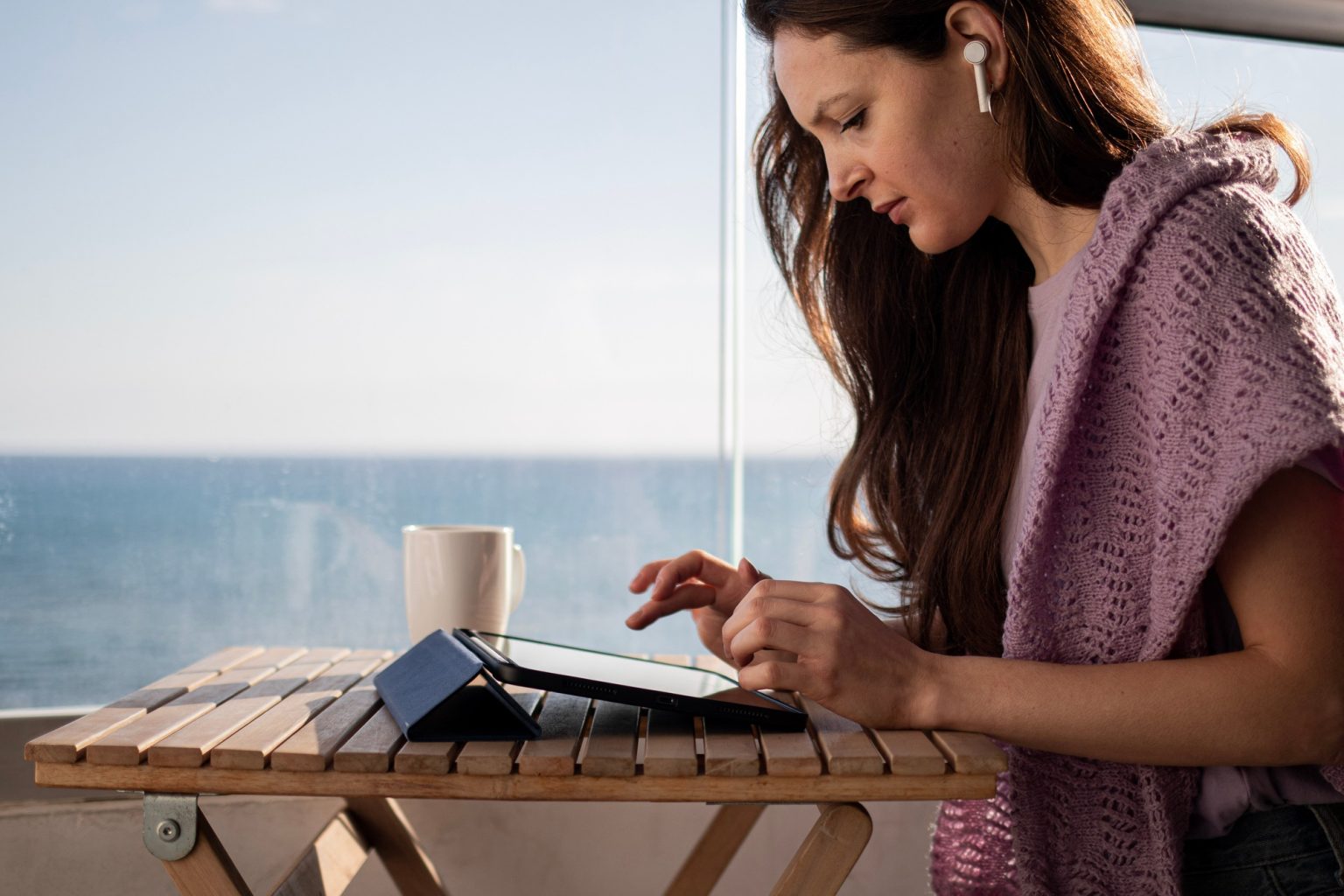Young woman in headphones is checking email on tablet on balcony on vacation
