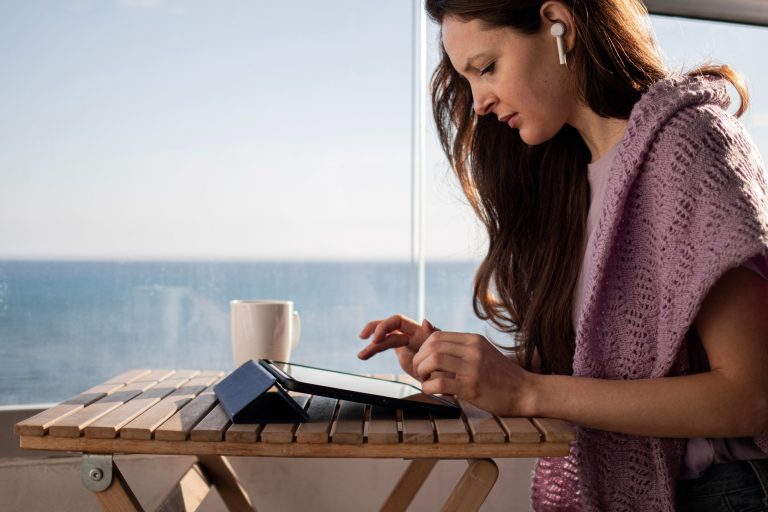 Young woman in headphones is checking email on tablet on balcony on vacation