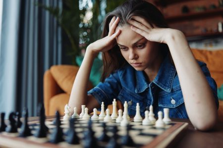 Guide complet pour maîtriser le jeu du Mastermind Woman contemplating her next move in intense chess game at table, head in hands, deep in thought