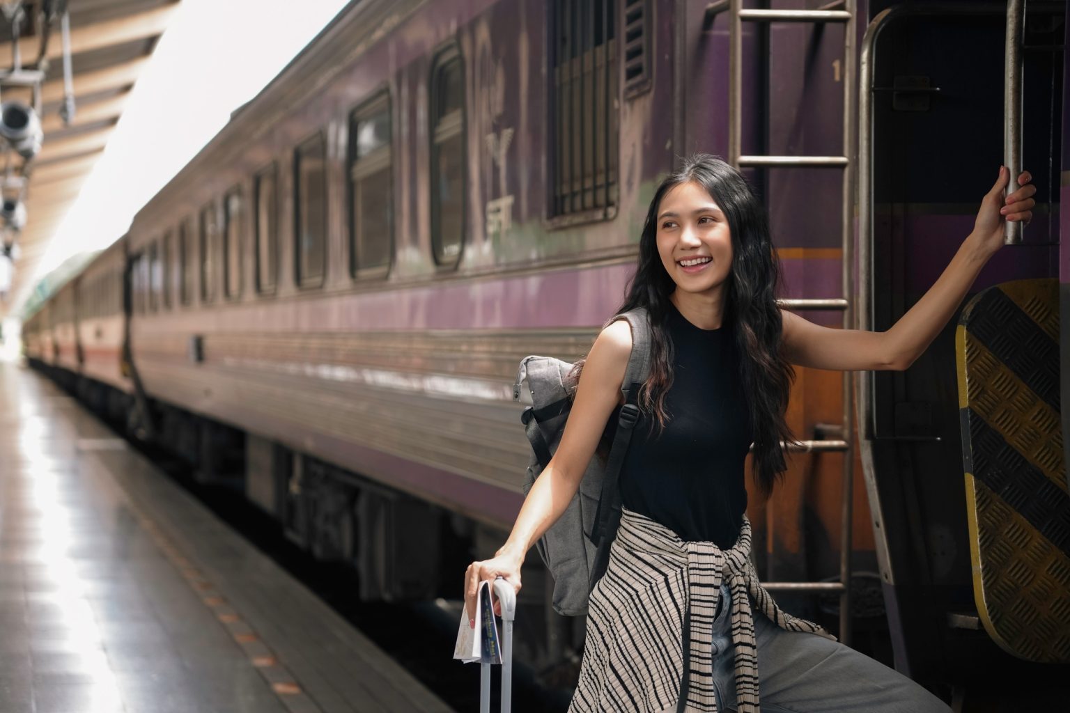Young woman is boarding a train for her travel, she is smiling and holding the handrail