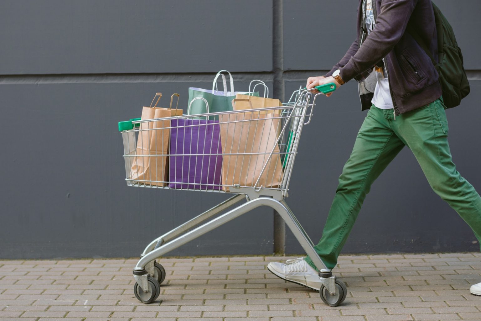 Comment choisir le meilleur chariot de course pour faciliter ses achats quotidiens ? A man in bright trousers rolling a shopping cart.