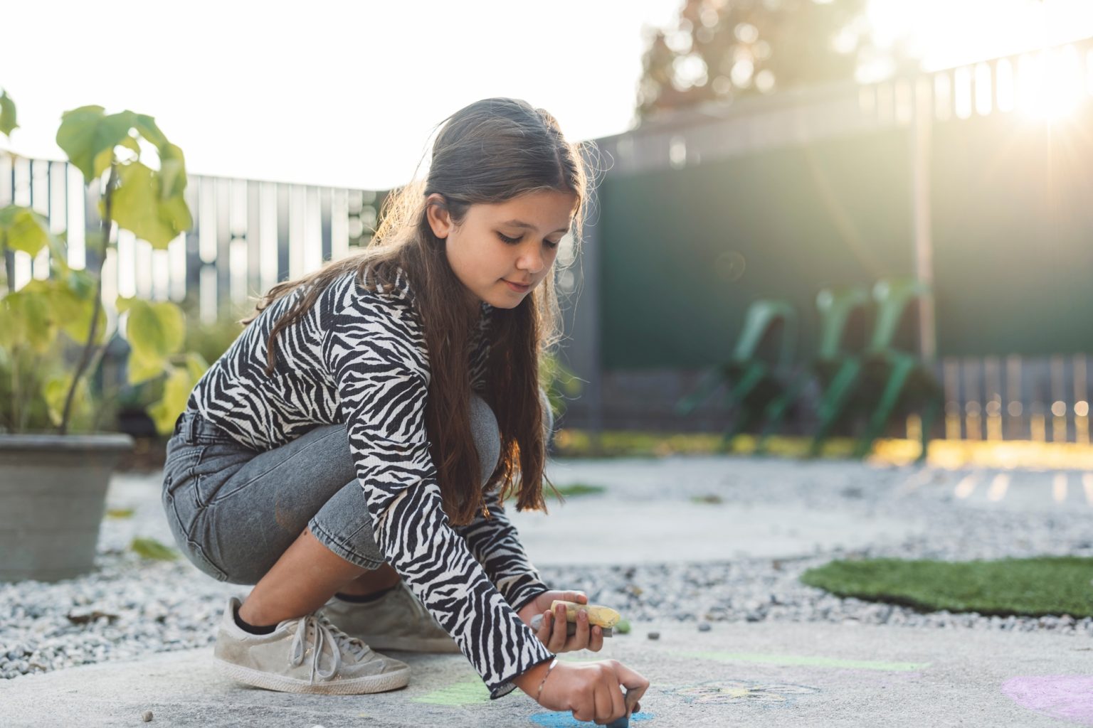 A young girl with long hair, wearing a zebra-striped shirt and shorts, is crouching down and drawing