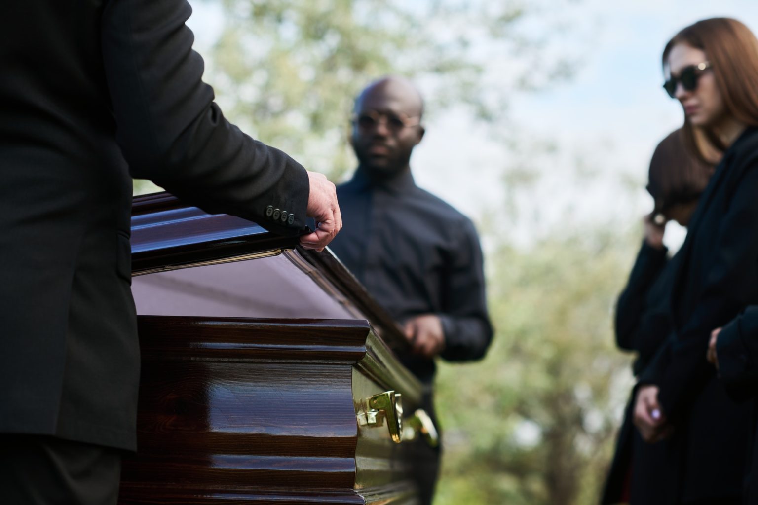 Close-up of man in black suit closing lid of coffin at funeral ceremony