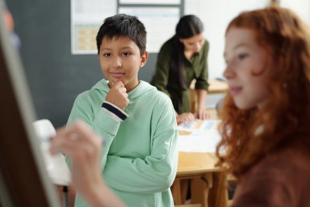Focus on pensive schoolboy looking at grammar rules on whiteboard