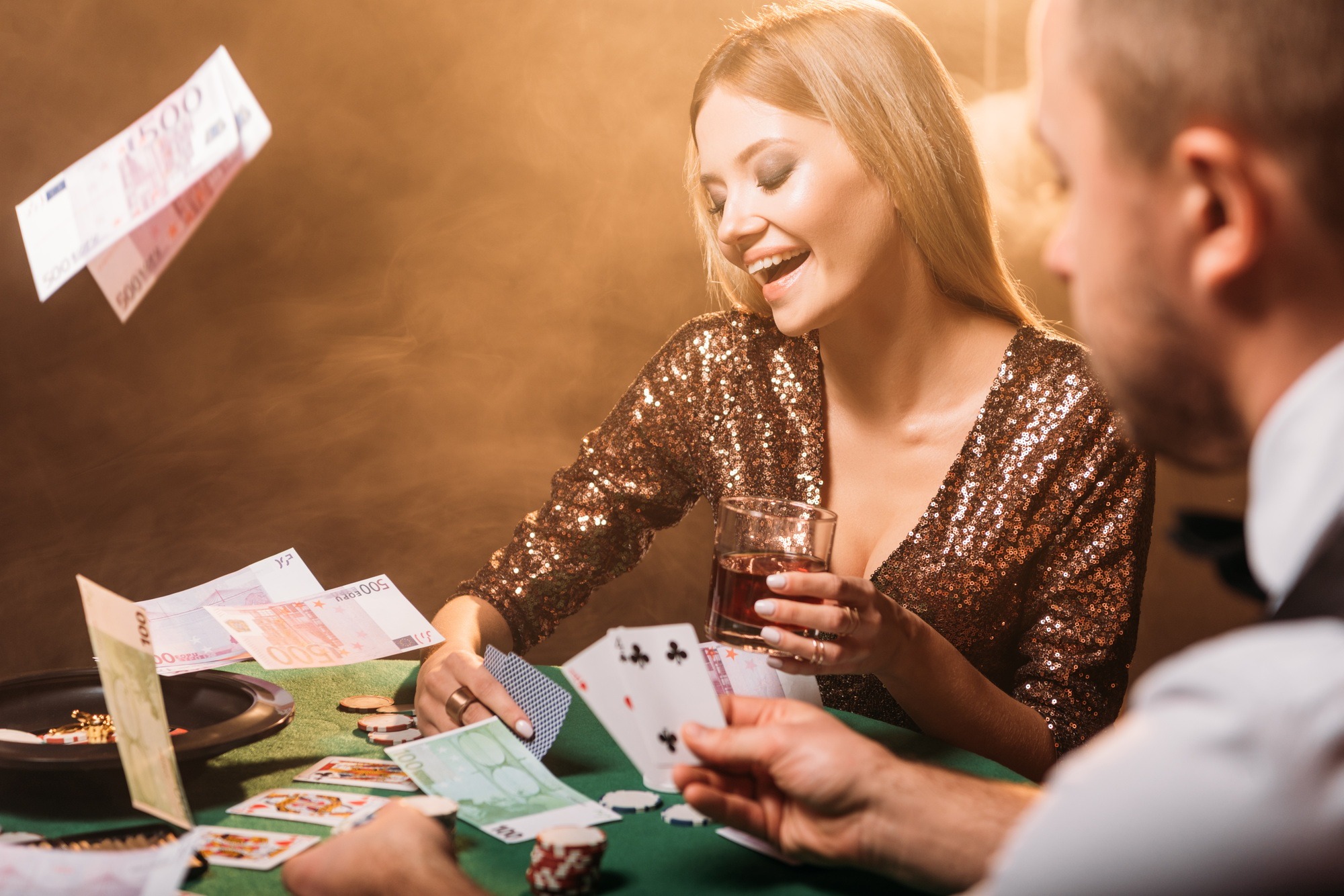 happy attractive girl playing poker with croupier at casino, euro banknotes falling on table