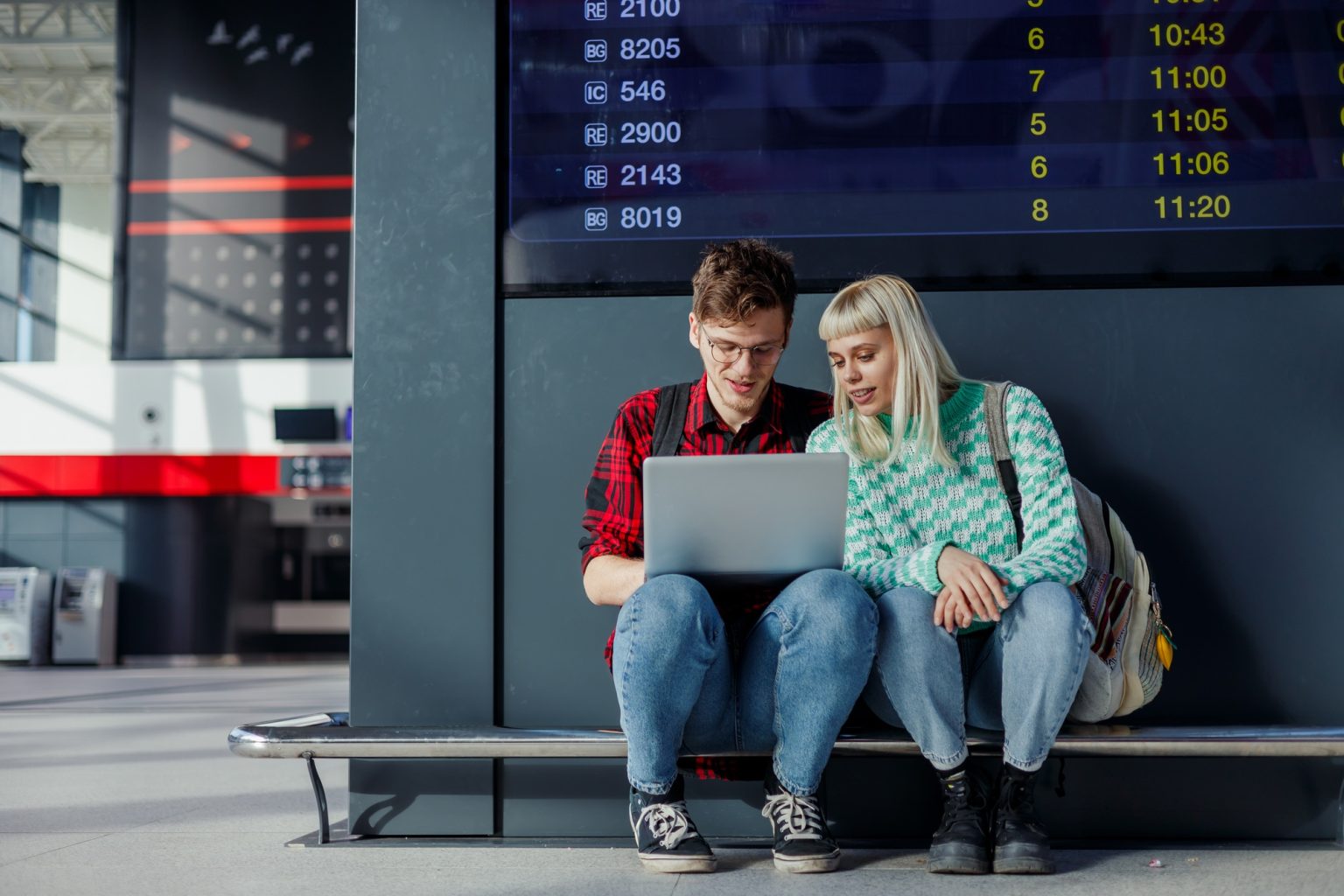 Young traveling students sitting at train station and using a laptop.