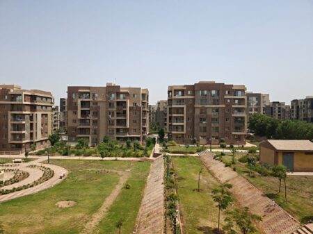 Aerial view of modern apartment buildings surrounded by lush greenery on a sunny day.
