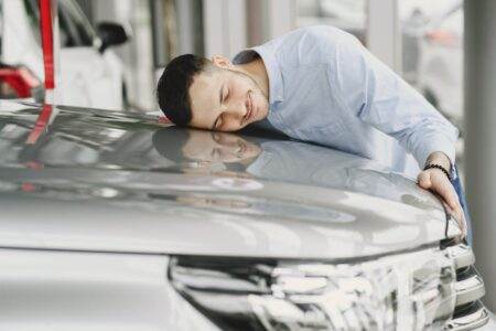 Leasing auto : LOA ou LLD, quelle formule choisir en 2026 ? A man joyfully embracing a new car indoors, reflecting happiness and satisfaction.