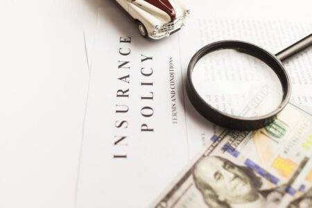 Suppression de la carte verte d’assurance auto : ce qui change vraiment pour les conducteurs Close-up image of an insurance policy with a magnifying glass, money, and toy car.