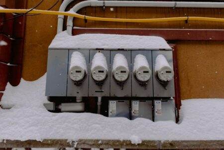 A row of electric meters covered in snow during winter, illustrating infrastructure resilience.