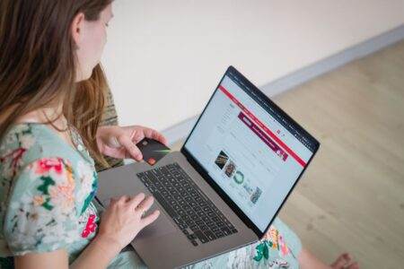 Numéro de téléphone : la fin des contraintes géographiques bouleverse la donne pour les fixes Woman in floral dress shopping online with a laptop and credit card indoors.