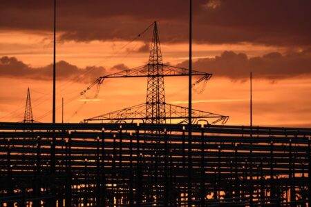 Silhouetted electric tower against vivid sunset sky, highlighting urban infrastructure.