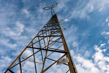 A detailed low-angle shot of a power line tower extending into a cloudy blue sky.