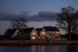 Peaceful rural houses overlooking a calm river under twilight skies, capturing serene countryside life.