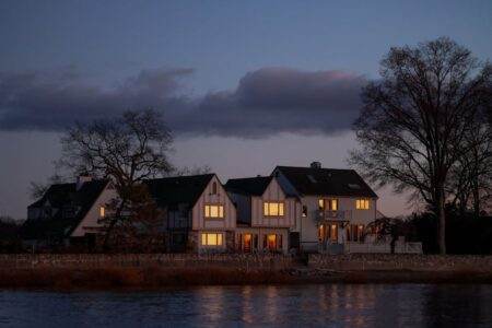 Peaceful rural houses overlooking a calm river under twilight skies, capturing serene countryside life.