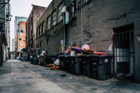 Prix d’un déménagement avec JeChange : démarches, coût et calendrier à retenir A gritty urban alley in Seattle with overflowing trash bins and high-rise buildings.