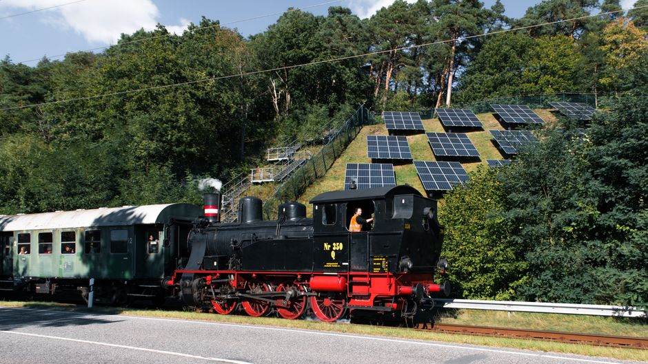 Hausse du gaz en mars 2026 : ce qui vous attend et comment réagir Historical steam locomotive beside modern solar panels, blending nostalgia with technology.