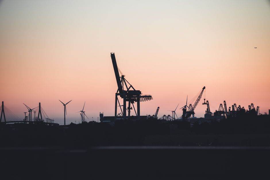 Arnaque des faux agents EDF à la porte : les 7 erreurs qui vous coûtent très cher Silhouetted cranes and wind turbines at the port of Hamburg during sunset, highlighting industrial beauty.