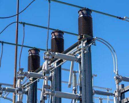 Detailed view of electrical components in a power substation under a clear blue sky.
