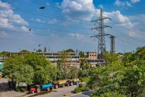 A vibrant aerial shot of an industrial area in New Delhi with power lines and trucks under a bright sky.