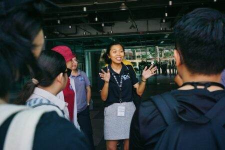 Aides Action Logement pour déménager en 2026 : ce qui existe encore, ce qui a disparu, comment en profiter Tour guide leading a group tour, engaging visitors with gestures in an outdoor urban setting.