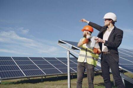 Alerte EJP : deuxième jour rouge consécutif, ce qui change pour votre facture Young businessman in formal outfit and foreman in yellow vest looking away while discussing working process against solar panels