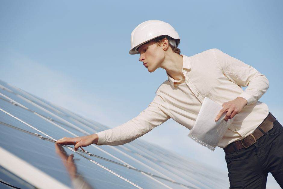 Chèque énergie 2026 : calendrier, deuxième vague d’envoi et pièges à éviter Low angle of young male inspector with documents in formal wear and hardhat standing against solar panels and checking details of construction