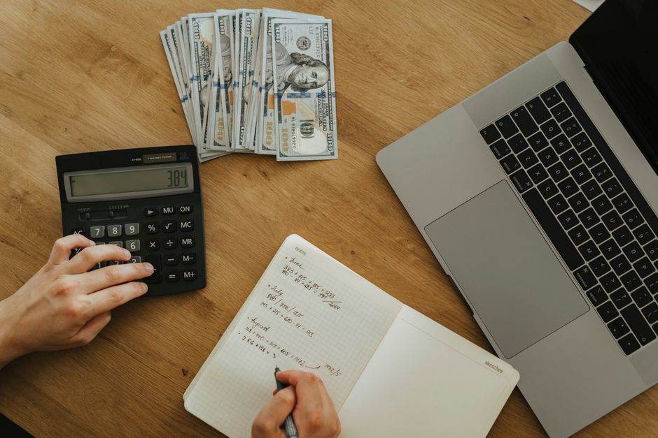 Person checking savings account on laptop with bank passbook and calculator