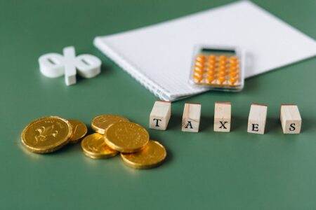 Baisse des taxes sur l’électricité en 2026: ce que vous gagnerez vraiment selon votre facture Close-up of tax-related items including coins, calculator, and word 'taxes' on a green background.