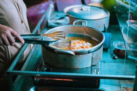 Quel appareil de cuisine consomme 60 fois plus d’électricité que votre frigo ? La réponse en chiffres Close-up of a person frying food in a pan using tongs on a stove indoors.
