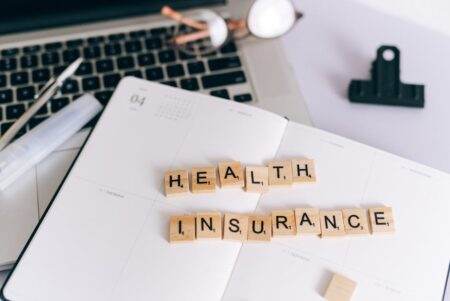 Loi Lemoine : comment elle a fait exploser le jeu de l’assurance emprunteur Close-up of Scrabble tiles spelling 'Health Insurance' on a planner with a laptop.