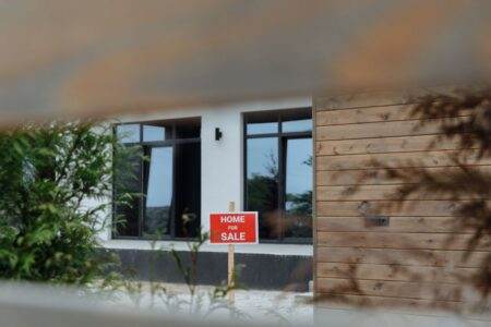 Obtenir le meilleur taux immobilier en 2024-2026 : les leviers concrets que les banques regardent vraiment A contemporary home with a 'For Sale' sign in the front yard, framed by greenery.